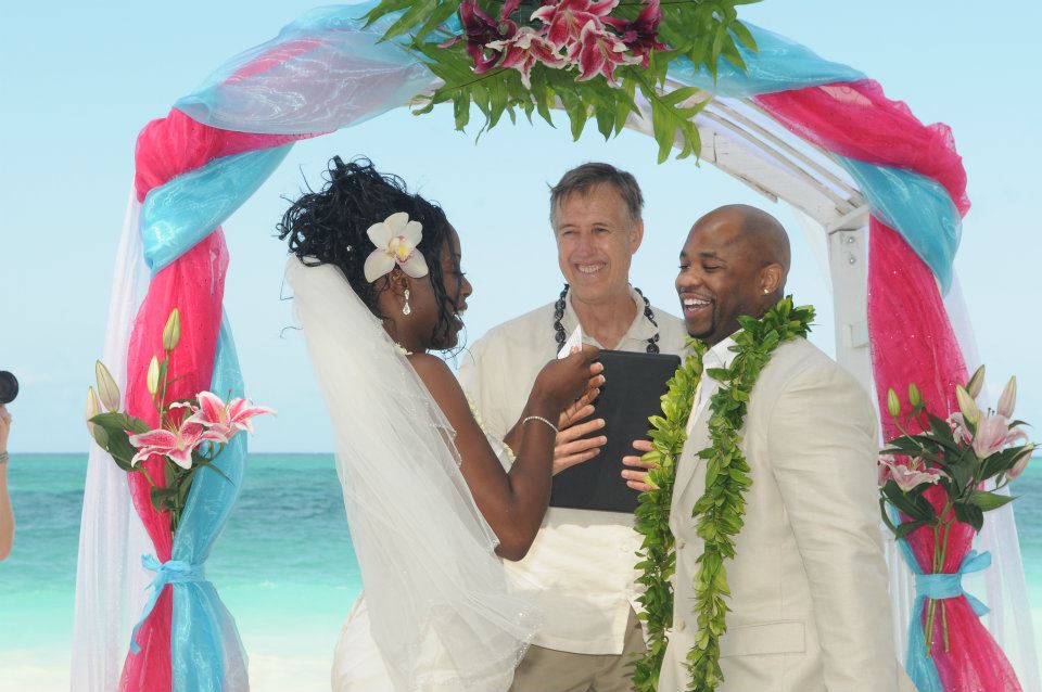 Minister Chris Cain smiling with the couple as they say their vows under a pink and blue arch
